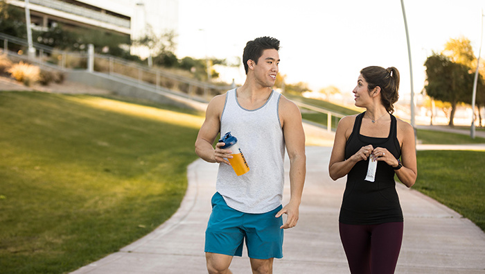 Man and woman talking while holding a bottle of liquid and opening a protein bar wrapper.