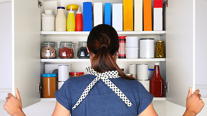 Back of woman, who is looking at her cabinet of groceries.