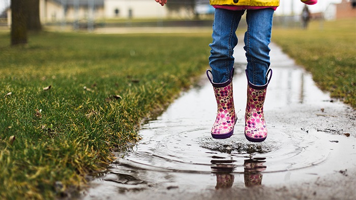 A close-up of a child's pink flower galoshes as they jump in a rain puddle