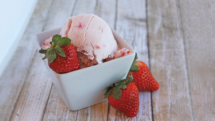 Bowl of strawberry ice cream with strawberries.