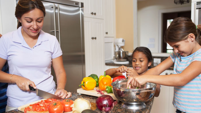 Two girls preparing vegetables in the kitchen with their mother