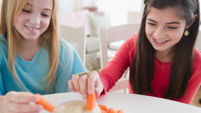 Two girls dunking carrots in dip