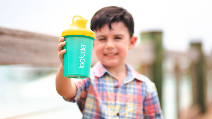 Young boy in a colorful plaid shirt holding up a yellow and teal IsaKids® shaker cup