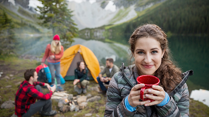 Woman holding mug while she and her friends camp by the lake