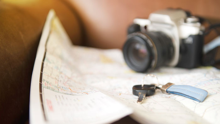A camera and car key resting on a road trip map
