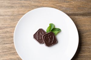 Two Dark Chocolate With Mint Flavor IsaDelight squares on a plate with mint leaves