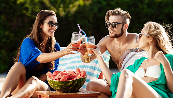 Three friends sunbathe and clink glasses while on vacation