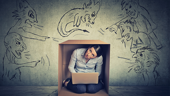 Woman kneeling in a cardboard box intimidated by criticism and self-doubt