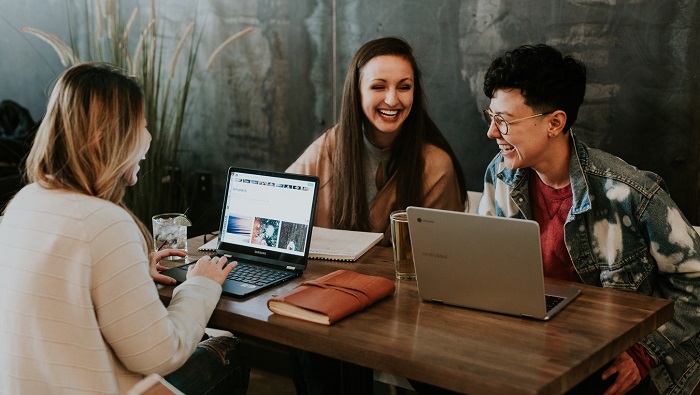 Three young adults laugh while working on laptops at a table