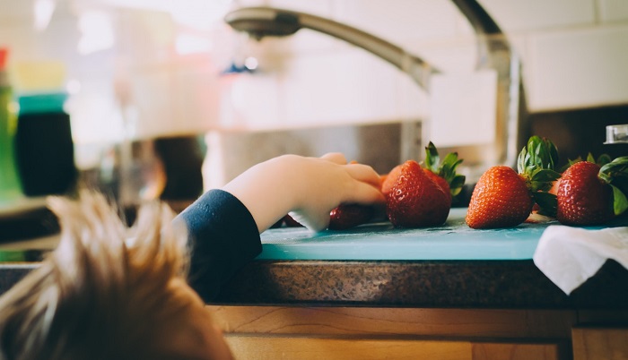 Child reaching for a strawberry on the counter.