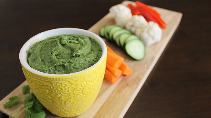 A bowl of hummus on a board of carrots, cucumbers, cauliflower, and bell peppers.