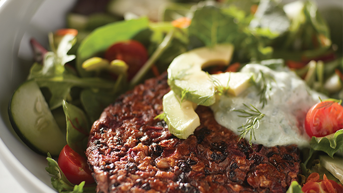 A bowl of veggie burger with black beans, lettuce, cucumbers, avocado, and tomatoes.