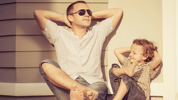 Father and son relaxing in the sunshine with their arms behind their head