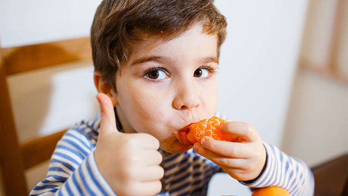 Young boy eating a tangerine while giving a thumbs-up.