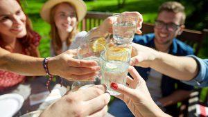 Five friends sit outside and clink glasses of water with orange slices in them