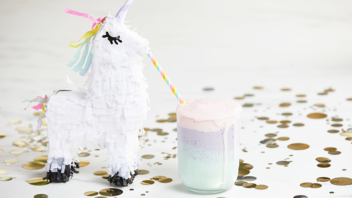 Mini unicorn pinata drinking a pink, lavender, and light blue protein shake with a rainbow straw.