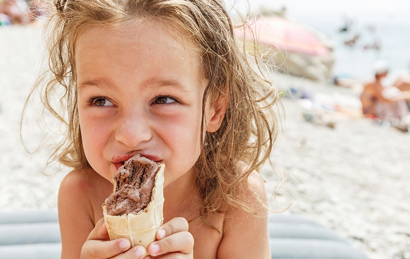 Child on the beach eating a chocolate ice cream cone