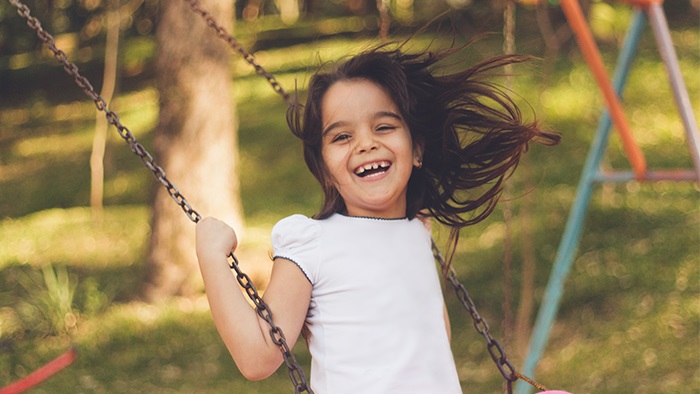 A little girl with brown hair smiling while swinging