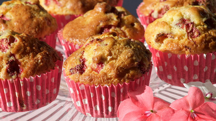 Strawberry muffins in red polka dot wrappers with flowers on the side.
