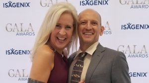 Husband and wife Brent and Tracey Shaw smiling in front of the Isagenix Gala Awards wall