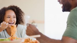 Child eating noodles with her father