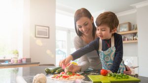 A mother making veggie pizza with her son in the kitchen
