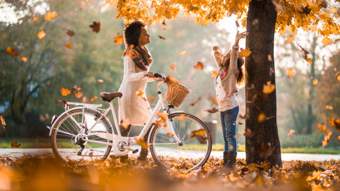 A woman walking her bike as autumn leaves fall