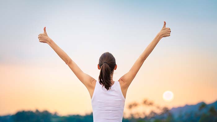 Woman holding two thumbs-up while looking at the sky