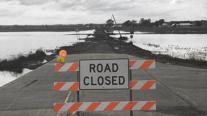 Sign that says Road Closed on traffic barrier on a road surrounded by water.