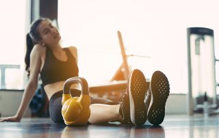 A woman sitting on the gym floor with a kettlebell
