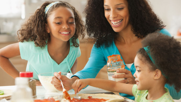 A mother and her daughters putting sauce on pizza