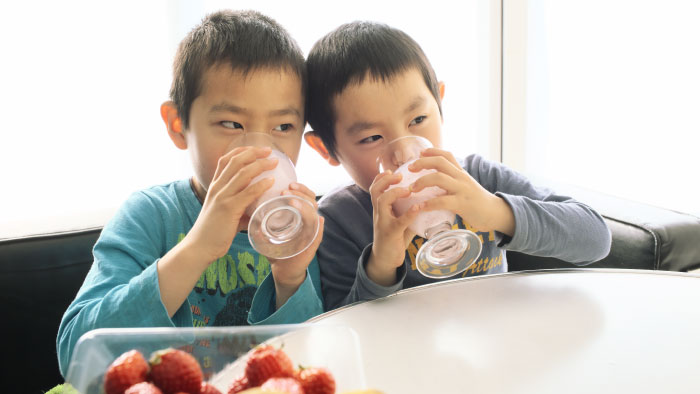 Two boys drinking strawberry smoothies from glasses