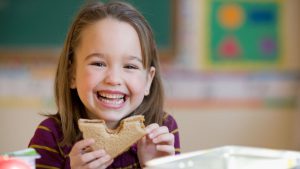 A little girl eating a peanut butter and jelly sandwich