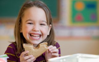 A little girl eating a peanut butter and jelly sandwich