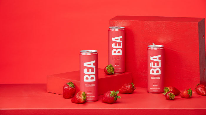 3 cans of Berry Bellini BĒA Sparkling Energy Drink against a red backdrop