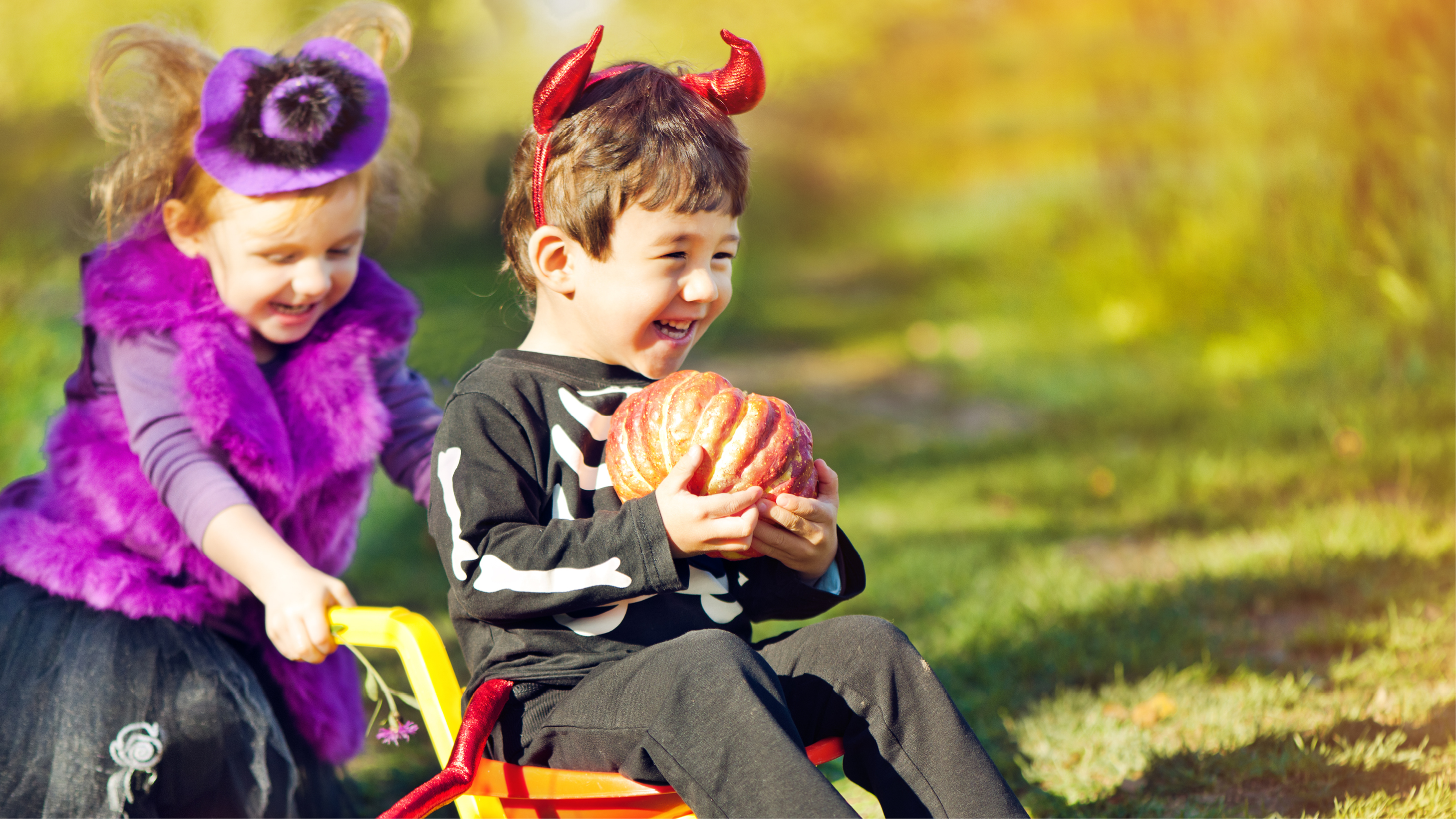 Two kids dressed up in costumes playing and holding a pumpkin