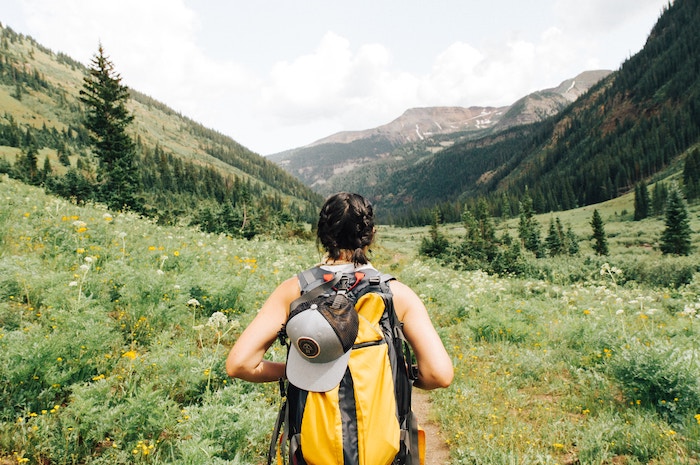 Photo of woman's back with her hat and backpack as she hikes through greenery