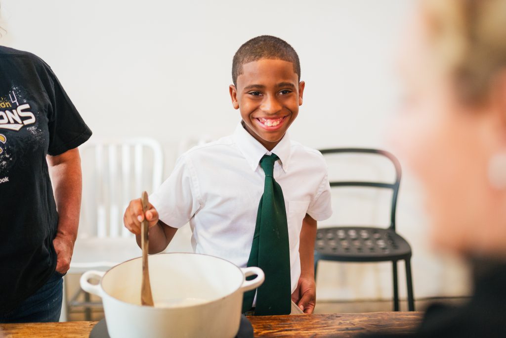 A child smiling and stirring a pot of food