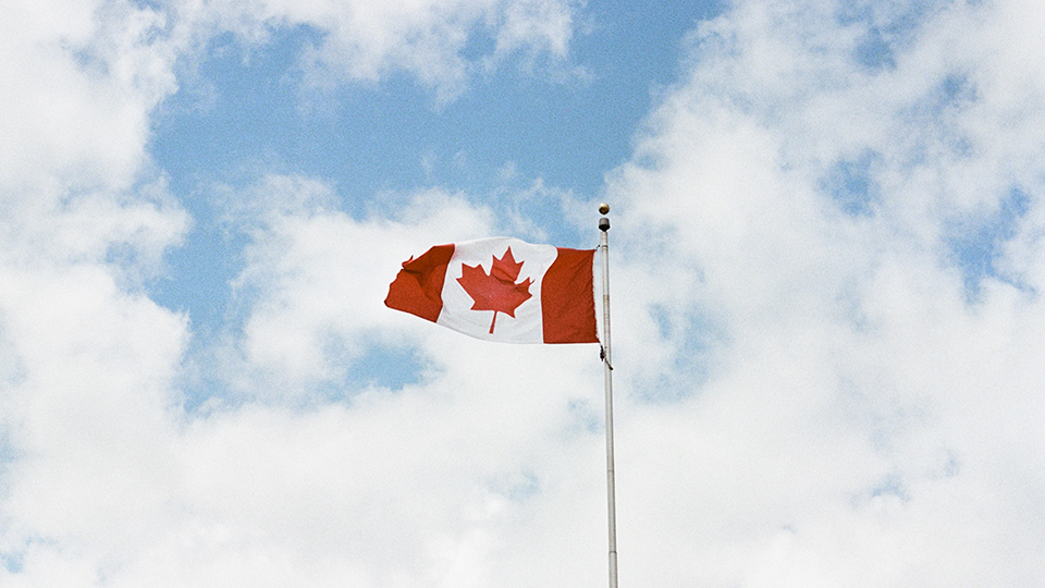 The Canadian flag flying in a cloudy blue sky