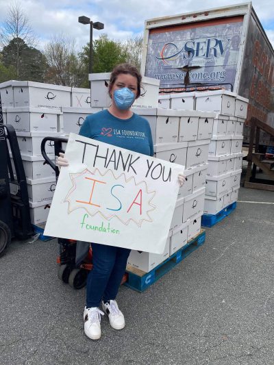 A woman in a face mask holding a "Thank You ISA Foundation" sign