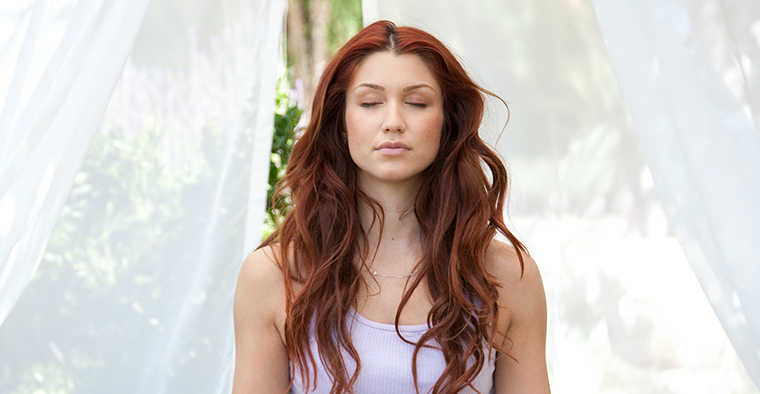 A woman with long red hair with her eyes closed in meditation