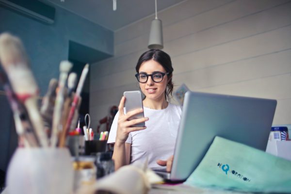 Woman with glasses sitting at a desk and looking at her smartphone