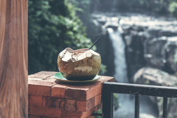 An open coconut with a straw sitting on a brick ledge
