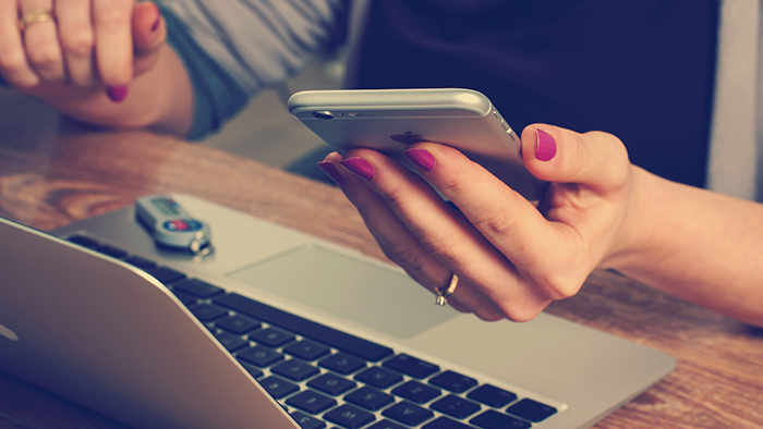 Manicured hands holding cellphone over a laptop