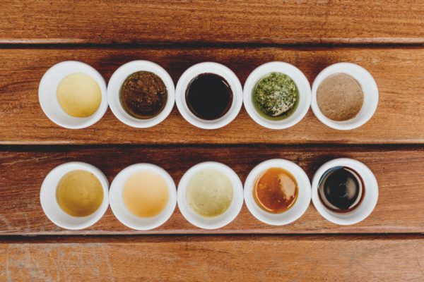 Ten sauces in little white bowls lined up in two rows on a wood table