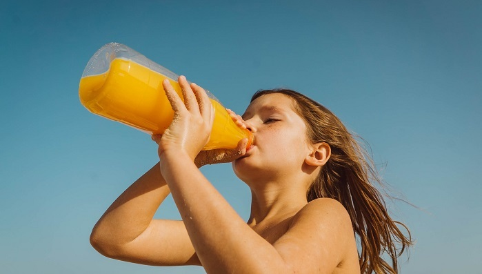 Young girl drinking bottle of orange juice