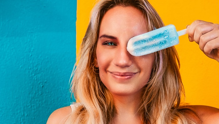 Woman holding blue popsicle over eye