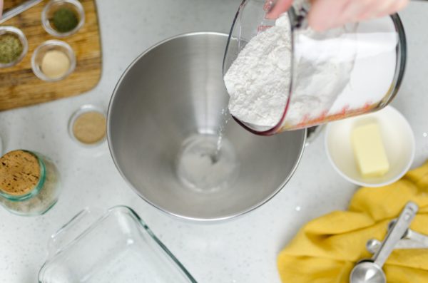 A person pouring white flour into a metal bowl