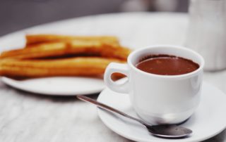 Churros on a white plate and chocolate sauce in a white mug