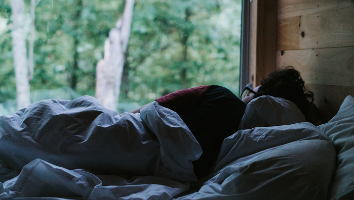 A person asleep under the covers facing toward a window